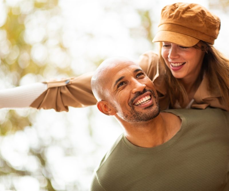 Happy man carries his partner on his back as she stretches out her arms, embracing the excitement of the moment.