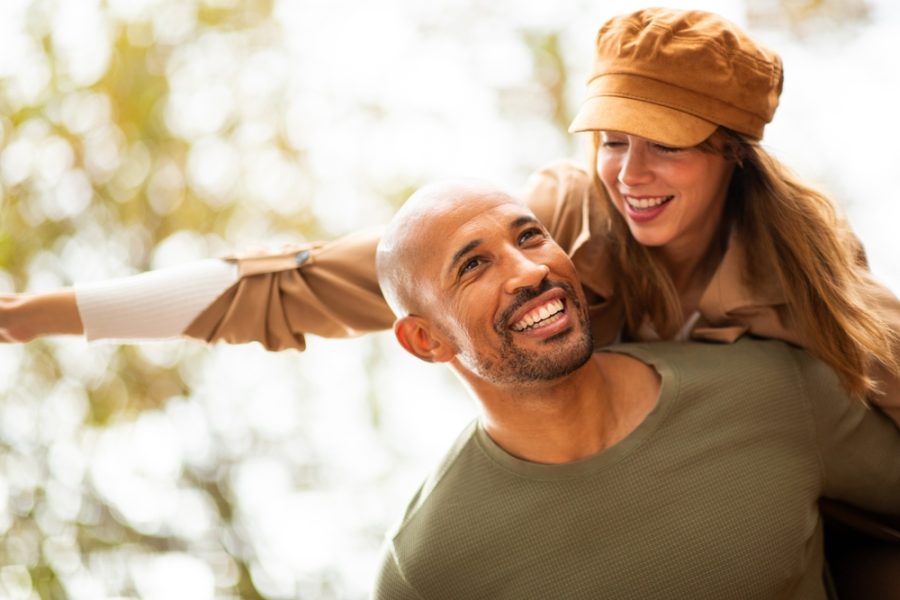 Happy man carries his partner on his back as she stretches out her arms, embracing the excitement of the moment.