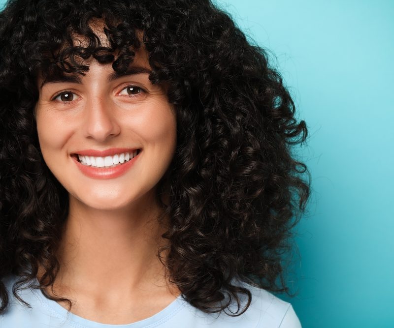 Happy young woman on light blue background. Dental veneers
