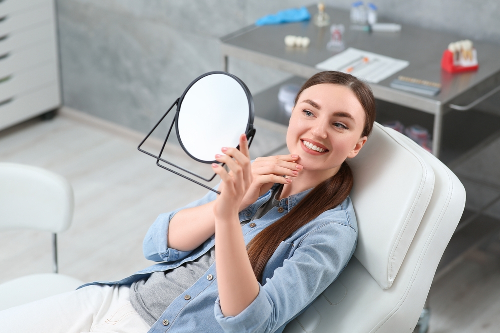 Reviewing Results of Cosmetic Dentistry Treatment – Cosmetic Dentistry A patient smiling while holding a mirror after treatment, highlighting satisfaction and enhanced appearance from cosmetic dentistry – Cosmetic Dentistry