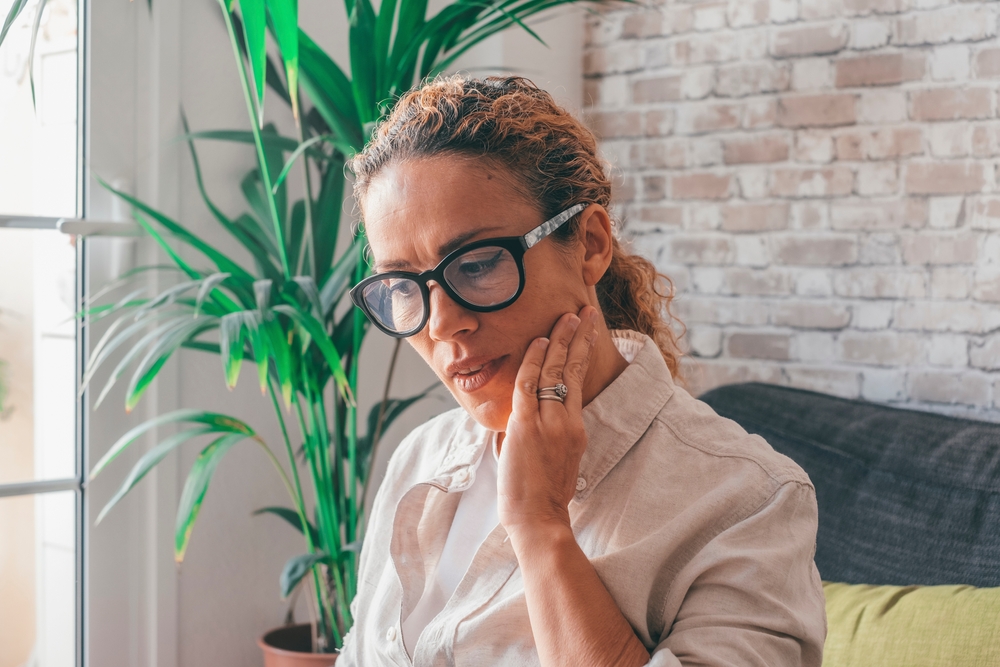 A woman holding her jaw at home, illustrating facial or tooth pain that may indicate the need for urgent emergency dental treatment – Emergency