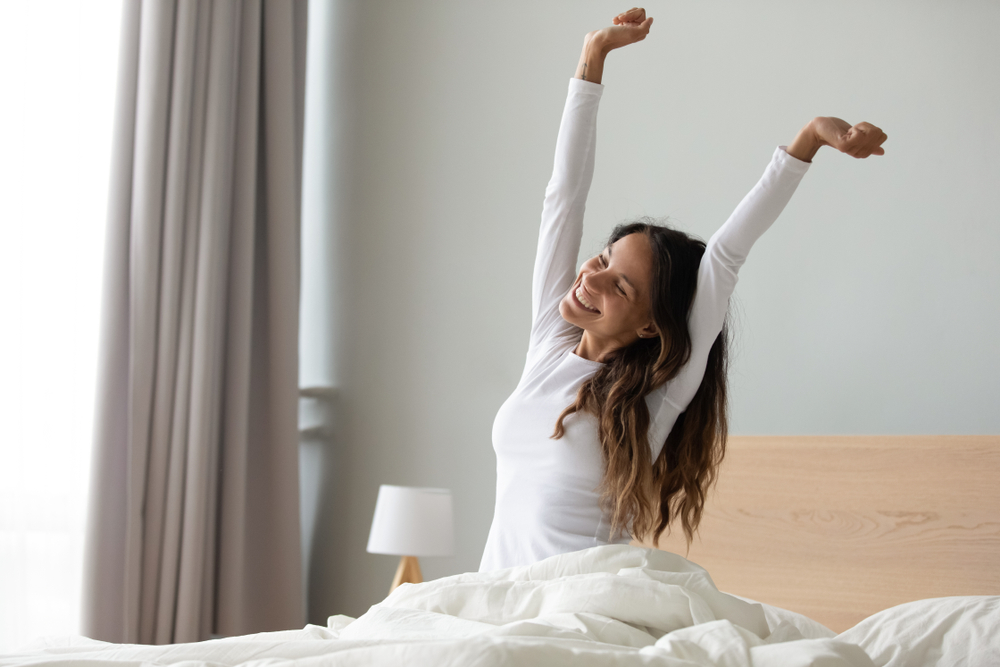 Waking Up Refreshed After Restful Sleep – Sleep Apnea A woman stretching and smiling in bed, representing improved energy and restorative sleep after effective sleep apnea treatment – Sleep Apnea