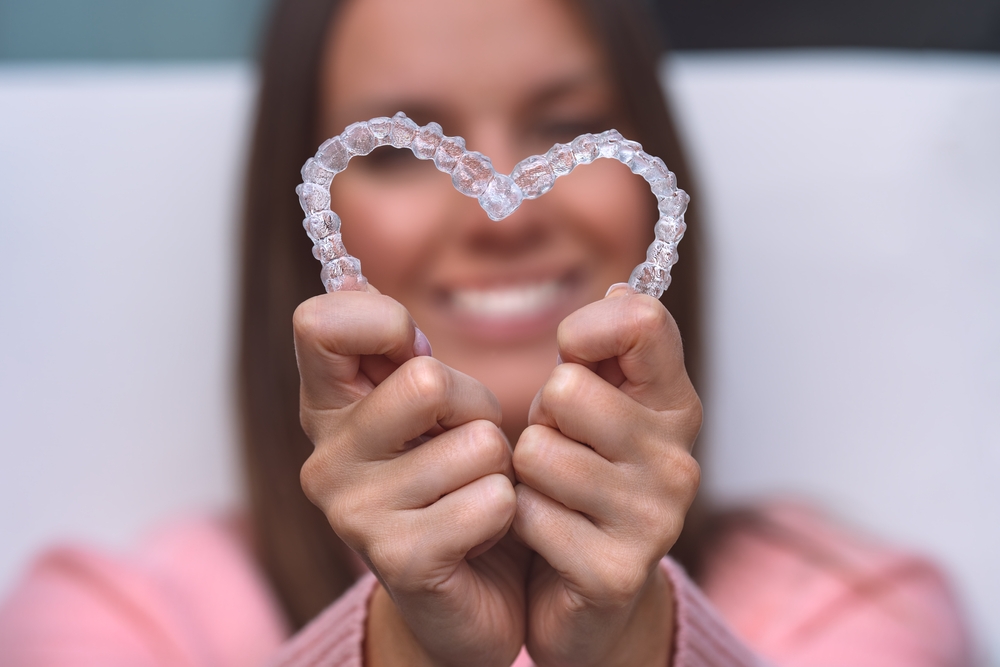 A patient holding clear aligners shaped like a heart, symbolizing advanced, discreet orthodontic solutions for straighter smiles – Orthodontics